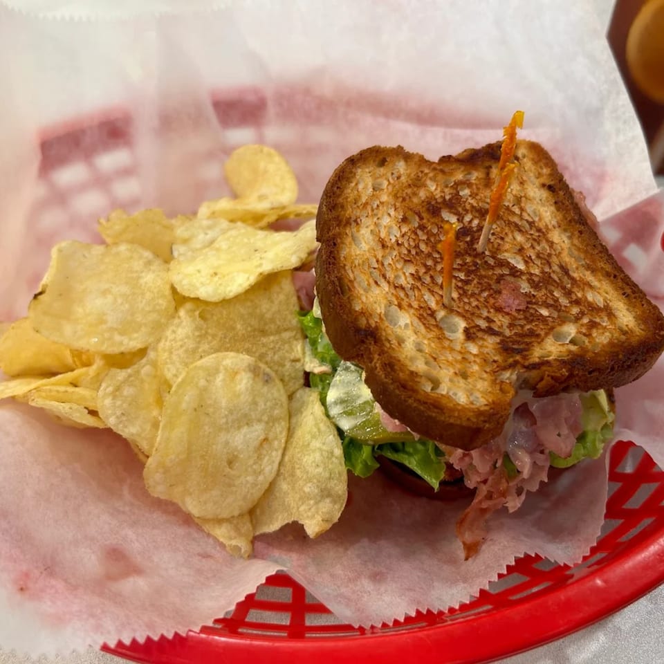 A Griddles Malt Shoppe diner sandwich with chips, served in a red basket lined with white paper.