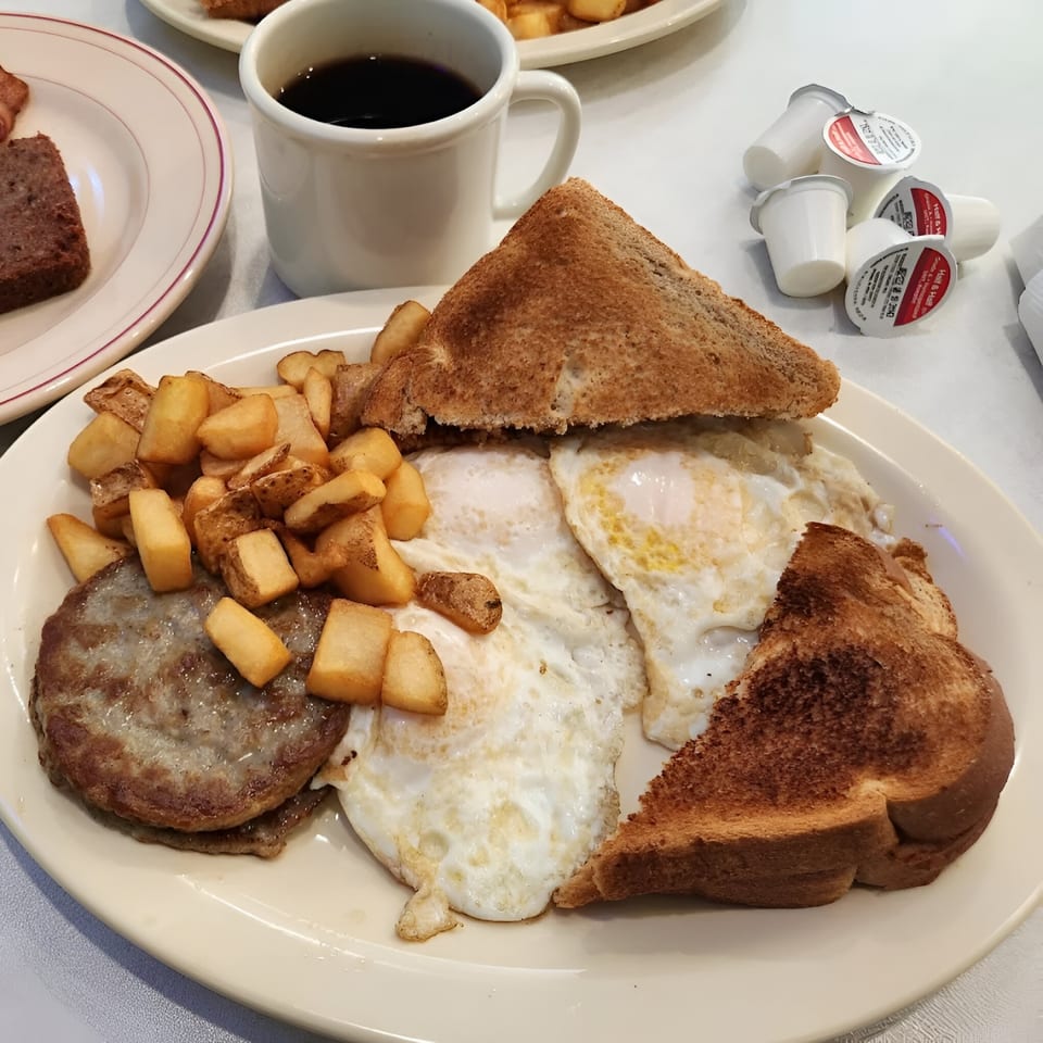 A diner breakfast plate with sausage patties, fried eggs, home fries, and toast, with coffee.