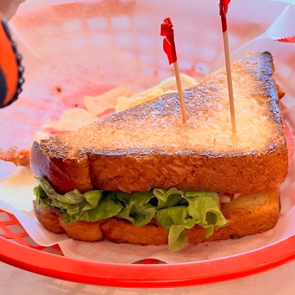 A grilled sandwich with lettuce and chips in a red basket at Griddles Malt Shoppe.