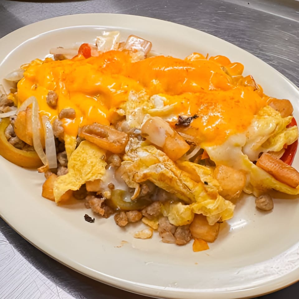 A diner breakfast skillet with eggs, potatoes, sausage, onions, peppers, and melted cheese.