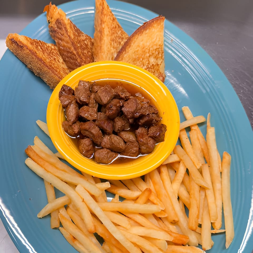 A blue plate with a yellow bowl of beef tips, a side of fries, and three pieces of toast.